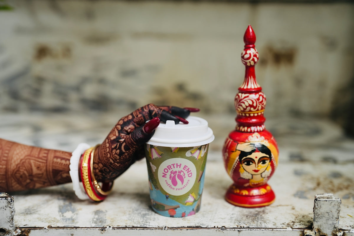 Woman's hand with henna next to decorated cup and bottle.